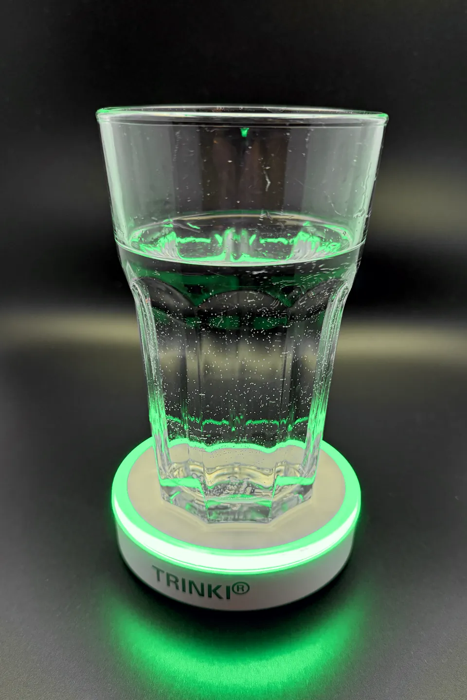 Ein Glas Wasser steht auf TRINKI, der Ring leuchtet grün und spiegelt sich auf dem Tisch